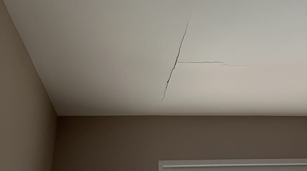 Fissure Plafond : Comment Diagnostiquer et Réparer Fissures structurelles en forme de T sur un plafond blanc à l'angle d'une pièce.