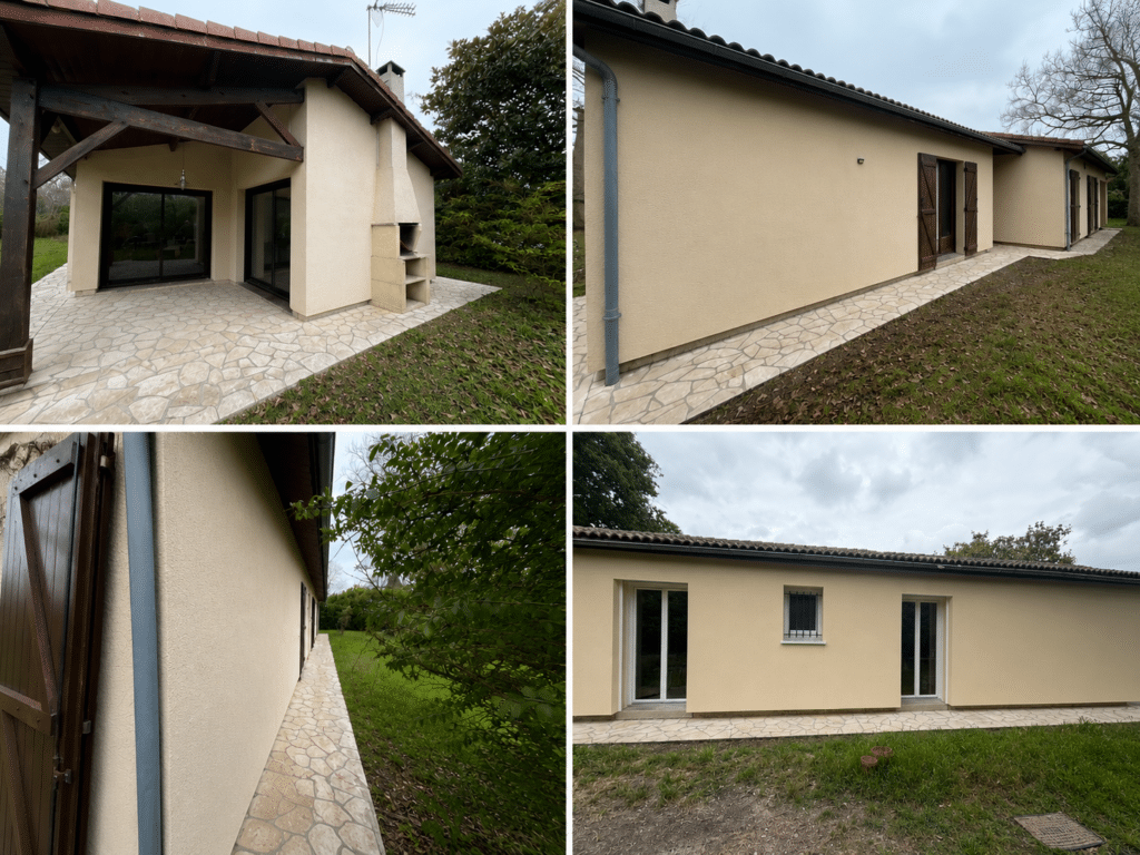 Maison beige avec terrasse en dalles, cheminée extérieure et volets en bois sombre sur jardin.